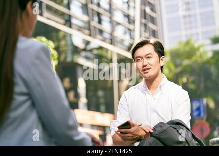 asian businessman and businesswoman conversing outdoors Stock Photo