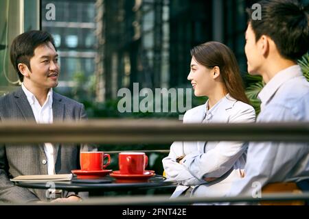 three asian corporate businesspeople discussing business outdoors in coffee shot Stock Photo
