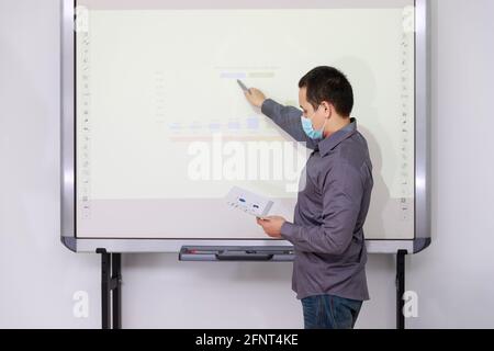 Businessman wearing protective masks present the monthly college budget in front of TV to his colleagues during meeting. Social distance practice prev Stock Photo