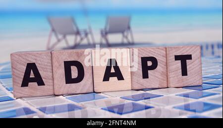 ADAPT Word on wooden blocks standing on swimming pool borders mosaic near the beach. Business change concept Stock Photo