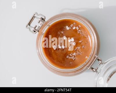 Salted caramel in glass jars, top view. Close up view of delicious brown caramel or condensed milk with sea salt crystalls. Light neutral background Stock Photo