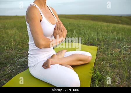 Girl yoga in nature. Crop woman meditating in summer spring countryside Stock Photo