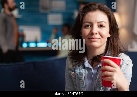 Portrait of beautiful woman holding beer glass looking into camera during night party. Multi-ethnic diverse group of friends gathered together to celebrate birthday late at night cheerful young people Stock Photo