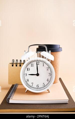 White alarm clock with arrows at nine in the morning and stationery made from recyclable material, coffee cup. Vintage watch on a beige background. Copy space. High quality photo Stock Photo