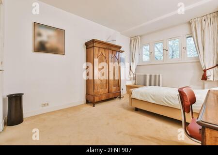 Lumber retro wardrobe located near comfortable bed in bedroom with small windows at home Stock Photo