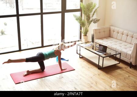High angle view of sportive mature blonde woman in sportswear having workout at home in front of laptop monitor Stock Photo