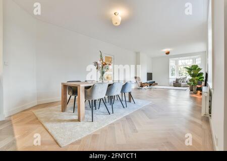 Minimalist style interior design of modern spacious light apartment with dining zone furnished with wooden table and comfortable chairs placed on carpet Stock Photo