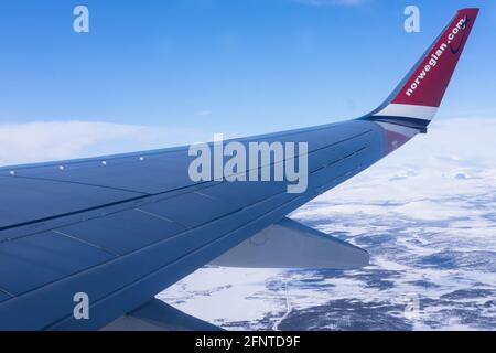 Wing of an airplane with blue sky above clouds. Logo of Norwegian Air on the wingtip Stock Photo