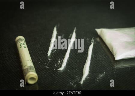 Drugs and dollars on glass, black table. Narcotic powder divided into stripes on a mirrored table, one hundred dollar tube for drug use Stock Photo