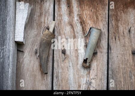Old, rustic sharpener rock for lawn mower against a wooden, red wall of a shed in a village Stock Photo