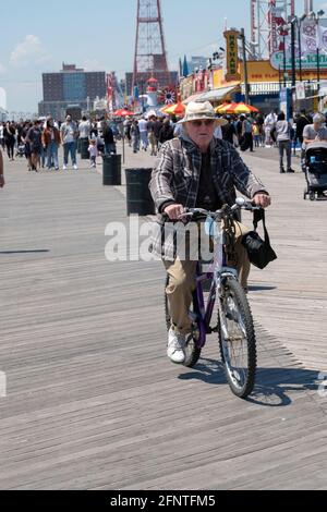 An older man wearing a wide brimmed hat rides his bicycle on the boardwalk in Coney Island, Brooklyn, New York City. Stock Photo
