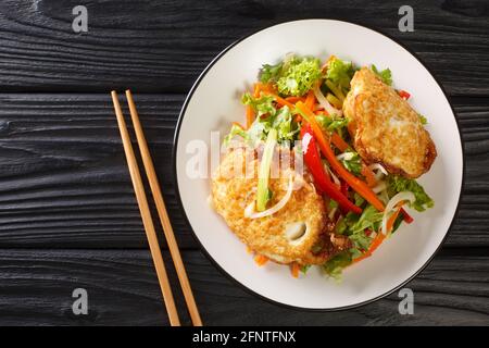 Asian salad of fried eggs with vegetables and herbs close-up in a plate on the table. horizontal top view from above Stock Photo
