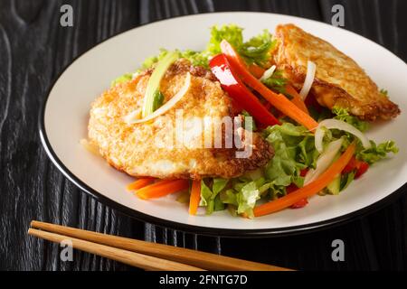 Asian salad of fried eggs with vegetables and herbs close-up in a plate on the table. horizontal Stock Photo