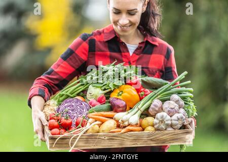 Beautiful dark haired farm woman holding the wooden basket full of fresh healthy homegrown vegetables from the garden. Stock Photo