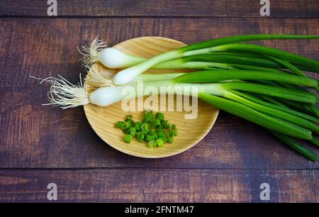 Whole raw Spring onions with roots and cut onions on a bamboo plate. Stock Photo