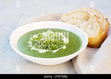 soup of fresh spinach with cream and arugula microgreen in a white plate with ciabatta bread on a light gray background. Healthy and diet food. Stock Photo