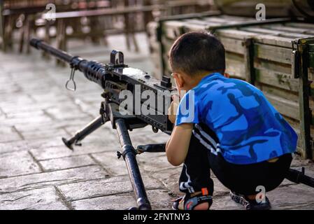 A little boy is playing with a model of a heavy machine gun Stock Photo