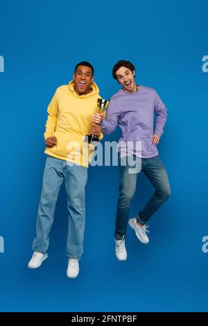 happy african american man with friend levitating and holding triumph cup  in hands on blue background Stock Photo