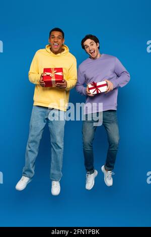 happy african american man with friend levitating with gift boxes in hands on blue background Stock Photo