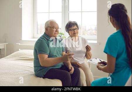 Worried senior couple sitting on bed and talking to nurse or family practitioner Stock Photo