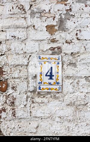 House number 4 in a flowery tile mirror on a whitewashed stone wall. The tile mirror consists of a main tile that is framed by four narrow tiles. Stock Photo