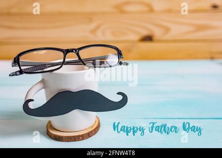 Happy Father's day concept. A black mustache paper, a cup of coffee and glasses on wooden table. Stock Photo