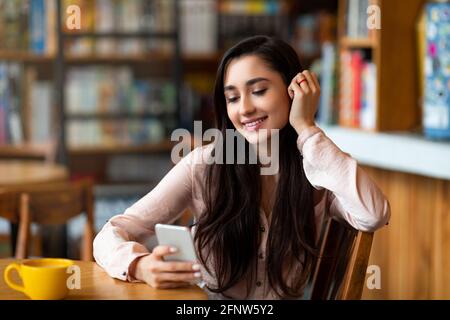 Happy arab woman using mobile phone, chatting with friends, using dating application or scrolling social networks feed Stock Photo