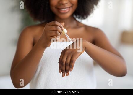 Closeup of feminine young black lady applying regenerating serum on her hands at home Stock Photo
