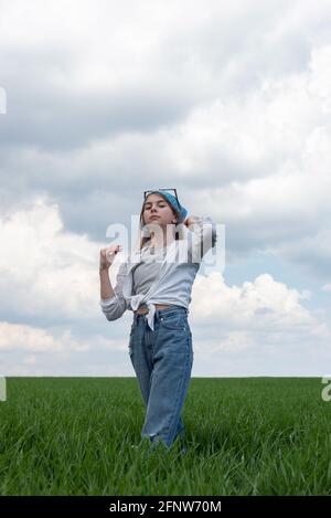 portrait of a little teenage girl in a field of green grass, against the backdrop of a cloudy sky. Stock Photo