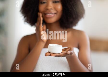 Domestic skin treatment concept. Cropped view of lovely black woman holding jar of facial cream at home, selective focus Stock Photo