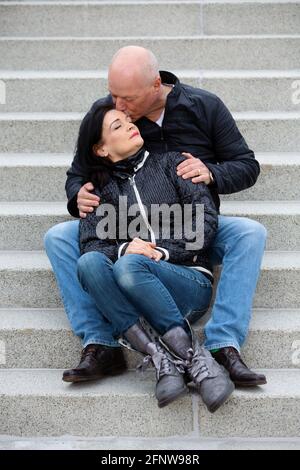 portrait of couple in their 50s sitting outside on steps and kissing Stock Photo