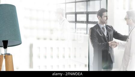 Composition of two smiling male doctors shaking hands in corridor with double exposure Stock Photo