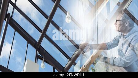 Composition of senior businessman and colleague shaking hands in meeting room with double exposure Stock Photo