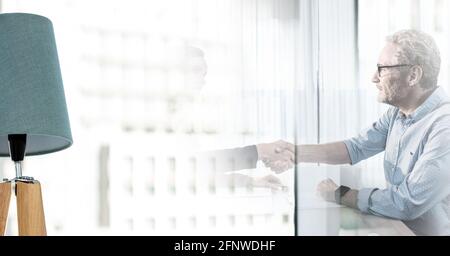 Composition of senior businessman and colleague shaking hands in meeting room with double exposure Stock Photo