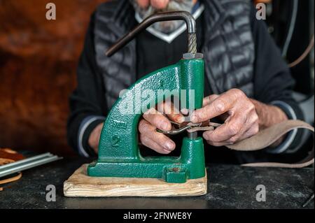 Closeup wrinkled hands of a senior man making holes in leather strap with puncher Stock Photo