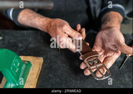 wrinkled hands of an old man showing a genuine leather belt. Italian handicraft. Stock Photo