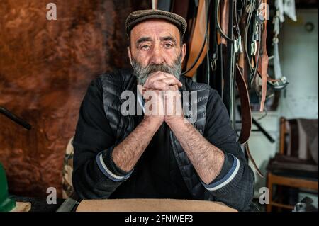 Portrait of old bearded hipster man looking at the camera with serious face. Craftsman working with genuine leather. Stock Photo