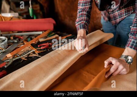 Unrecognizable craftsman working with piece of genuine leather in his workshop. Stock Photo
