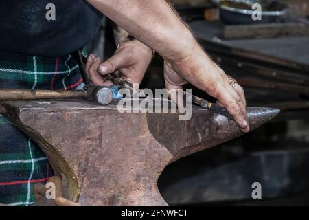 Blacksmith in kilts dirty hands - close-up - working metal on an anvil - selective focus Stock Photo