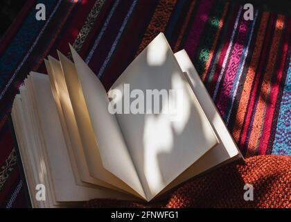 Image of an open notebook with blank pages laying on a table with a colorful tablecloth in the sun Stock Photo
