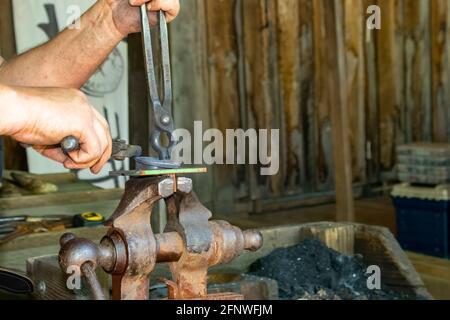 Blacksmith's hands at work at forge working with object held in vise with tongs at Oklahoma Renaissance Festival Muskogee Oklahoma 5 5 2018 Stock Photo