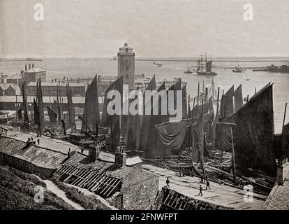 A late 19th Century view of the massed sails of the fishing fleet, tied up to the fish quay constructed in 1870 to provide shelter for the docked fishing boats in  Also pictured is the Low Light beacon remodelled in 1830 to serve as an almshouse. Stock Photo