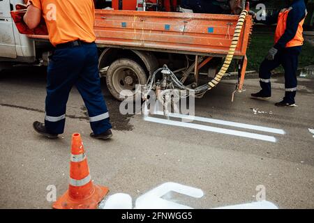 fresh marking of the pedestrian path on the asphalt. the workers painted the symbol of the man with white paint. orange cone warns of roadworks Stock Photo