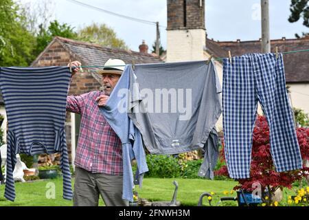 Man hanging washing on clothes line with pegs in the garden Britain, Uk. domesticated male drying outside exterior household chores jobs work men Stock Photo