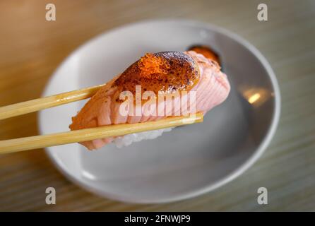 Salmon sushi grill top with sweet miso in chopstick by indoor low and warm lighting. Stock Photo