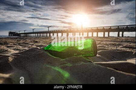 Green glass bottle waste on the beach with sunset lighting. Stock Photo