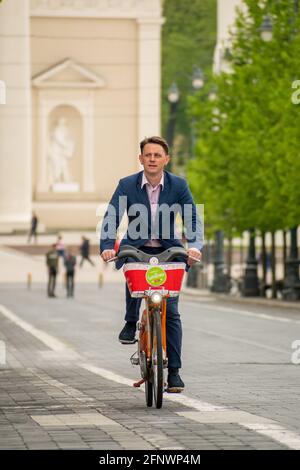 Business man in elegant dress or suit riding a bike on the road bike in the city center. Alternative and sustainable transport, vertical Stock Photo