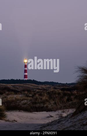 Historic lighthouse of Hollum with light beam, Ameland with a red and orange sky during sunset, sunrise. Dark dunes with stern grass in the foreground Stock Photo