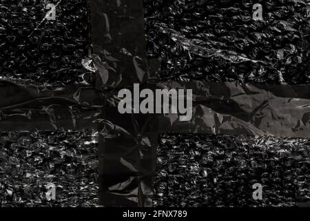 Black plastic bubble wrap packaging film with wrinkled adhesive tape. Close-up. Abstract dark background Stock Photo