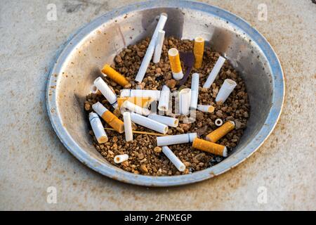 Close up of cigarettes butts in metal ashtray on street. Concept of many cigarette debris after smoking. Stock Photo